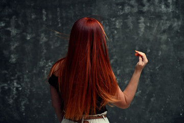 Obraz premium Red-haired Caucasian girl model with long curly hair on a gray background. Back view