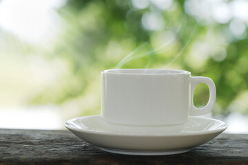 Close-up front view of a cup of tea Coffee with white saucers on a wooden table laid out in a green garden with morning sunlight gives a soothing feeling to start the day.