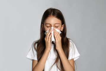 Little girl blowing nose into paper tissue on light grey background. Seasonal allergy
