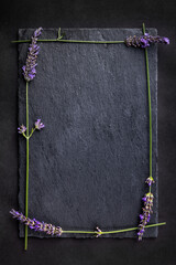 Top view of a black slate board with four lavender flowers around as a frame on a dark background. Romantic theme with copyspace for your text.