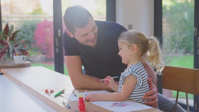Father and young daughter having fun at home sitting at table and painting decoration together - shot in slow motion