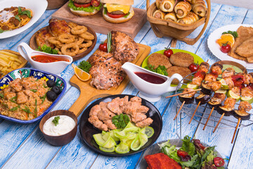 Wooden table full of delicious grilled bbq and fried food. Meat and vegetables. Summer picnic background. Delicious dinner.