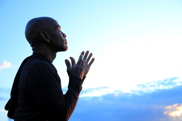 black man praying to god Caribbean man praying with blue sky in the background stock photo