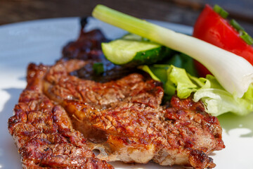 Meat steak with vegetables. A piece of fried meat with onions, tomatoes, cucumbers and lettuce leaves on a white plate. Selective focus