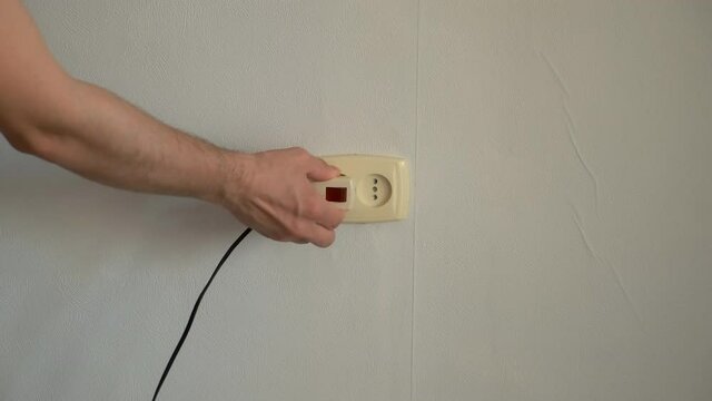 Man's hand turns off the plug into an outlet and puts on the red button. Electric extension cable with energy saving mode. Switching on fork to electrical socket on the wall at home..