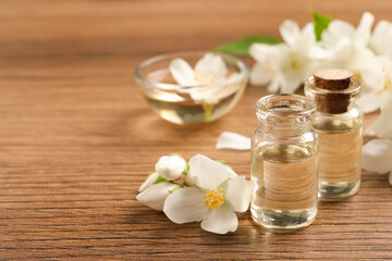 Fototapeta na wymiar Jasmine essential oil and fresh flowers on wooden table, space for text