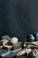 vertical still life photo on black background. The photo shows different types of bread and black jugs - 448726501