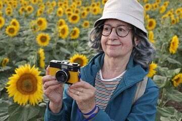 Senior tourist using vintage camera in sunflowers field