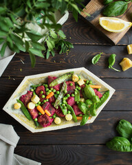 Italian cuisine. Beetroot gnocchi with parmesan cheese and lemon dressing. Healthy food on a brown wooden background. Vegetable side dish - green peas, carrots, mini corn