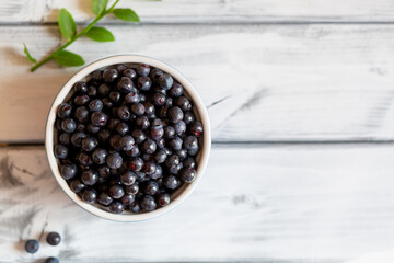 Blueberries in a blue cup and green leaves on a white table.Copy space. Selective focus