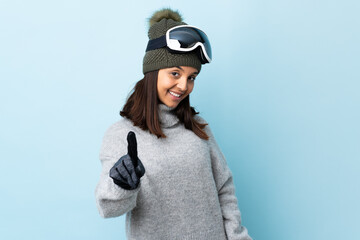 Mixed race skier girl with snowboarding glasses over isolated blue background showing and lifting a finger.