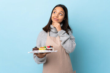 Pastry chef holding a big cake over isolated blue background thinking an idea while looking up.