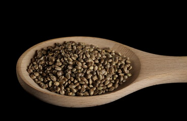 Hemp seeds pile in wooden spoon isolated on black background