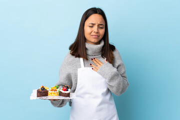 Pastry chef holding a big cake over isolated blue background having a pain in the heart.