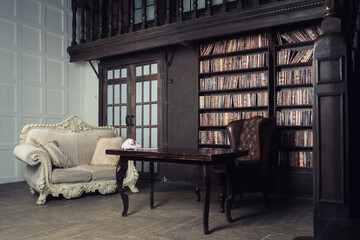 Classical library room with leather armchair, wooden table and bookcase.