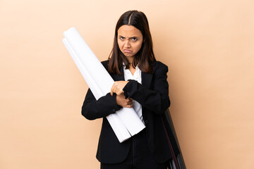 Young architect woman holding blueprints over isolated background making the gesture of being late