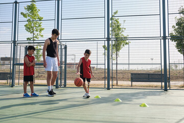 Basket trainer teaching two children how to play, one has a prosthesis.
