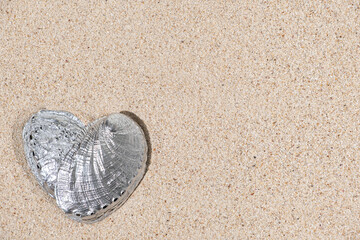 Fototapeta na wymiar Top view of heart shape silver color seashell on sand background with copy space