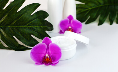 Moisturizing cream in a white jar with orchid flowers on white background. Natural cosmetics concept. Face and hand care cosmetics. Close-up. Selective focus.