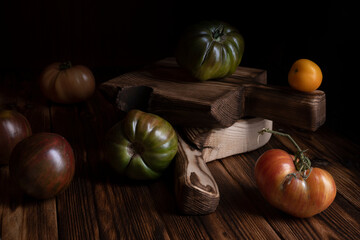 Red ribbed tomatoes on a beautiful wooden cutting board on a wooden background. Low key photo.