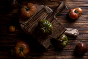 Obraz na płótnie Canvas Red ribbed tomatoes on a beautiful wooden cutting board on a wooden background. Low key photo.
