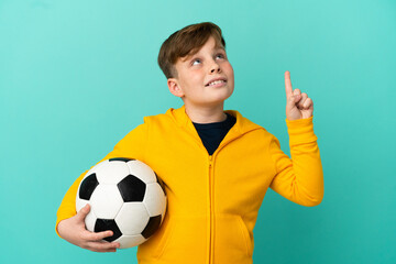 Redhead kid playing football isolated on blue background pointing up a great idea