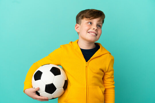 Redhead kid playing football isolated on blue background thinking an idea while looking up