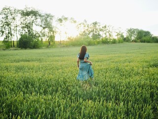 Happy woman in dress running in sunlight on summer field, enjoying life. Girl brunette long black hair fly in wind. Nature beauty, blue sky, field wheat. Freedom, Sustainable lifestyle, Wellness