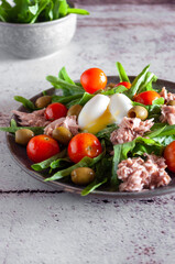 Salad with tuna, egg, lettuce, cherry tomatoes in a ceramic plate on a textured background in a minimalist style