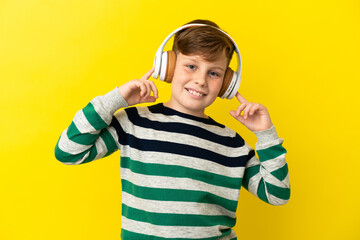 Little redhead boy isolated on yellow background listening music and singing