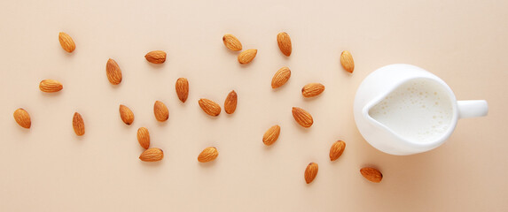 Almond alternative milk in a milk jug with almonds, top view, banner.