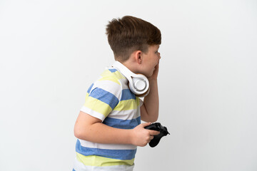 Little redhead boy holding a game pad isolated on white background shouting with mouth wide open to the side