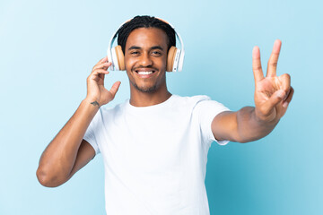 Naklejka premium Young African American man with braids isolated on blue background listening music and singing
