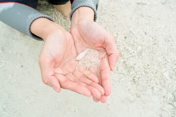 Close-up of a female wearing a wetsuit holding shell sand in both hands