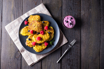 Vegetable vegetarian pumpkin pancakes with yogurt, blueberries and raspberries on a wooden background, summer food, delicious snacks. Pumpkin pancakes. Healthy food concept