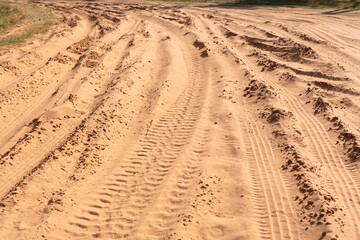 A fragment of a rural road made of loose pink sand. There are deep grooves and tread marks from passing vehicles. Background. Texture. 