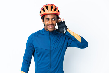 Young cyclist man with braids over isolated background listening to something by putting hand on the ear