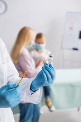 Pediatrician holding vaccine and syringe near blurred mother and kid