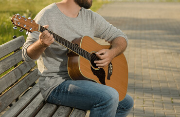 Guitar is in male hands, close-up. Caucasian man is sitting on a bench in outdoors and playing his...