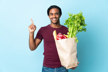 African American man holding a grocery shopping bag isolated on blue background pointing up a great idea