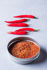 Red dried crushed hot chili peppers and chili flakes or powder in bowl on grey background.