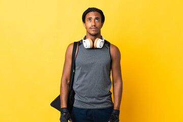 Young sport African American man with braids with bag isolated on yellow background and looking up