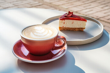 Cup of latte coffee with cheesecake outside.