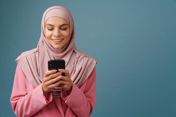 Young muslim woman in hijab smiling while using mobile phone