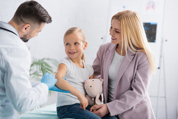 Obraz premium Smiling parent looking at kid near doctor with syringe during vaccination