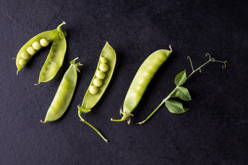 Pods of young green peas and peas on a black background close up