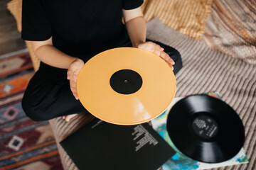 Young woman holding yellow vilyl record in a room with black wall decorated with vintage vinyl records.