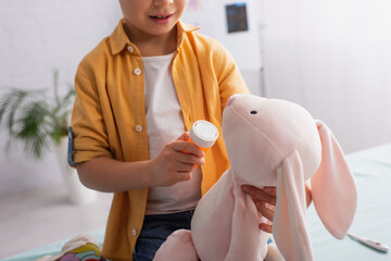 Cropped view of kid holding pills near soft toy and blurred thermometer in clinic