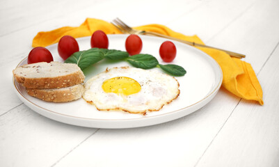 scrambled eggs with lettuce and cherry tomatoes on a white plate with a yellow napkin and golden cutlery