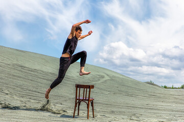 Young man in sportswear jumping over wooden chair against the background of sand dune